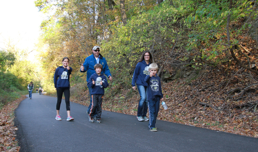 A family walks along a path at Sodalis Nature Preserve giving a thumbs up symbol to the camera