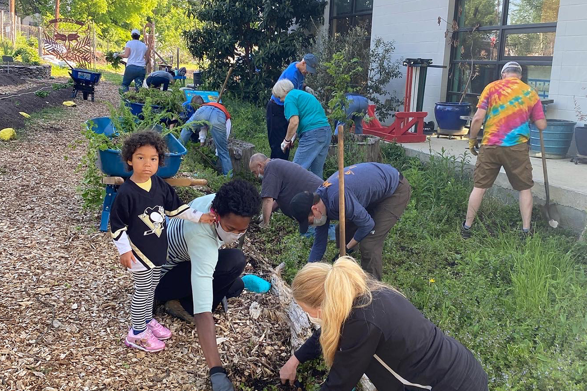 Many people bending over, planting seeds on the side of the road, with one child looking at the camera