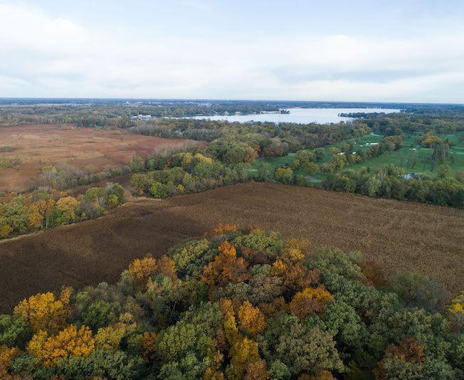 Large fields surrounded with trees and a lake in the background