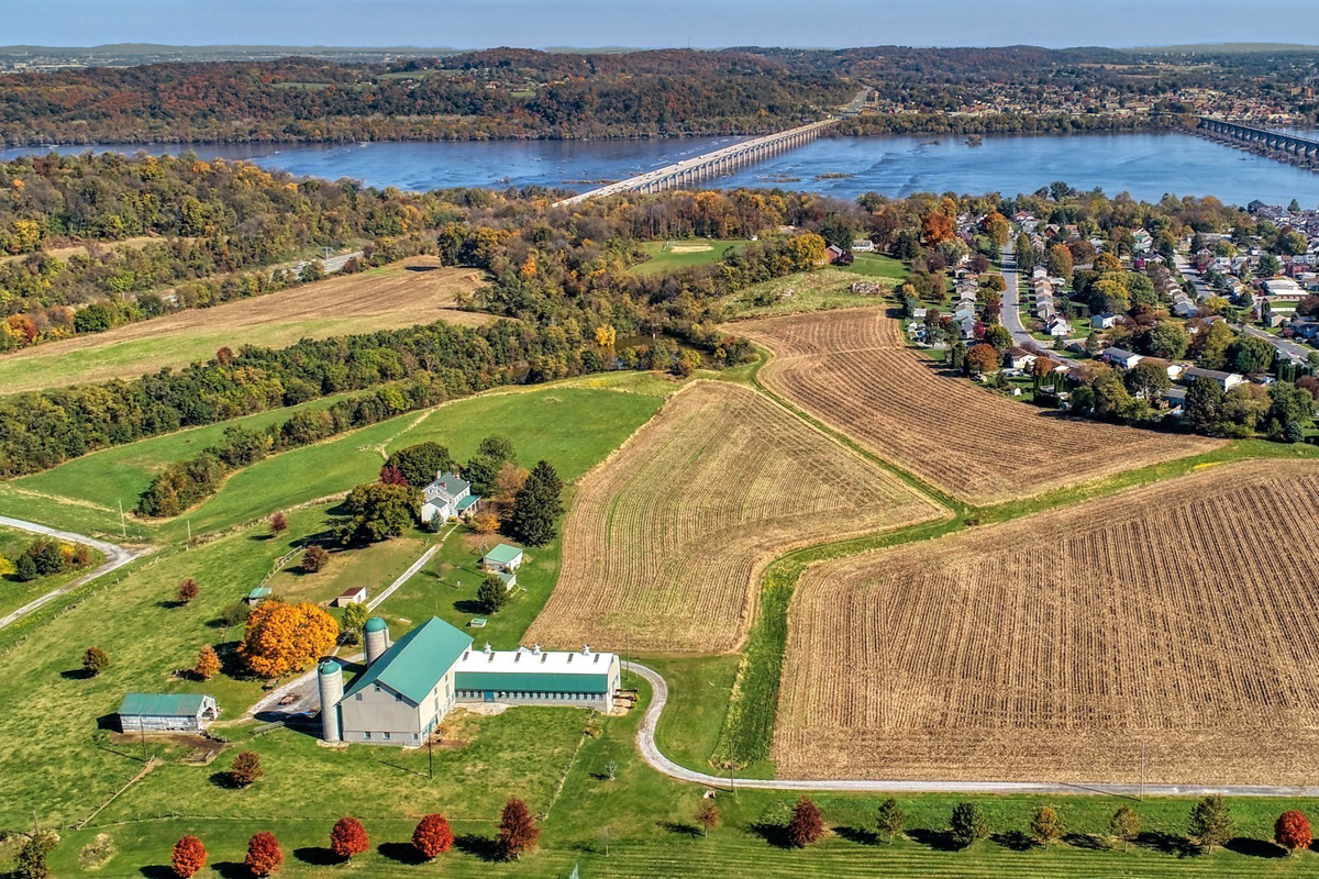 White barn buildings with teal roofs with farmland and houses and river in the background