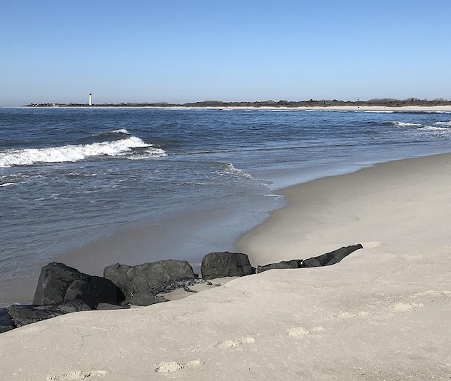 Sandy beach with ocean waves and lighthouse in the background