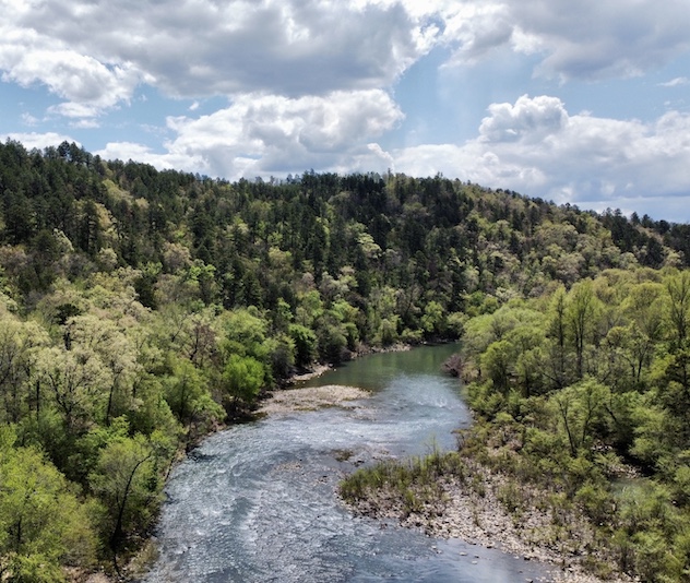 Winding river with trees on either side and white clouds