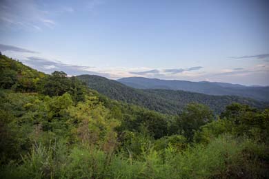 Mountains covered in green trees with sky in the background