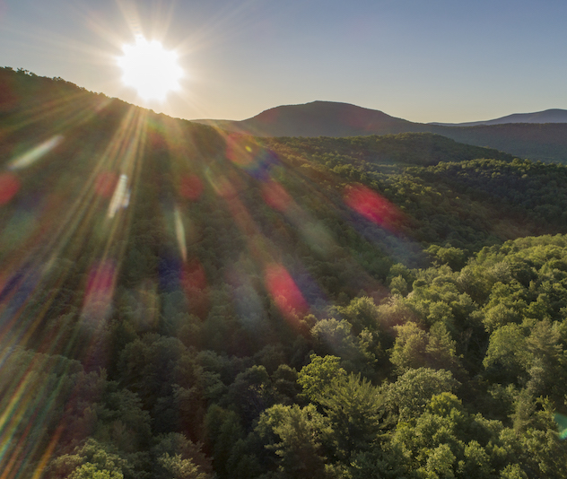 Sun peeking above tree covered hills