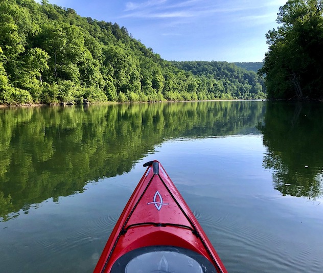 Red kayak on glassy river with green trees