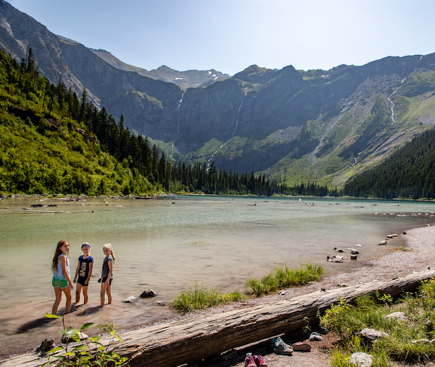 Three people standing in shallow water of a lake with mountains in the background